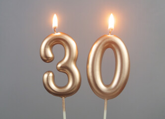 Burning gold birthday candles on gray background, number 30