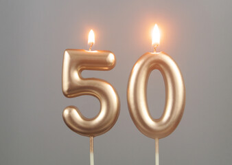 Burning gold birthday candles on gray background, number 50