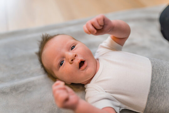 Indoor closeup portrait of a little infant baby boy clenching his fists and yawning with open mouth and eyes. Dark thin hair. Blurred background. High quality photo