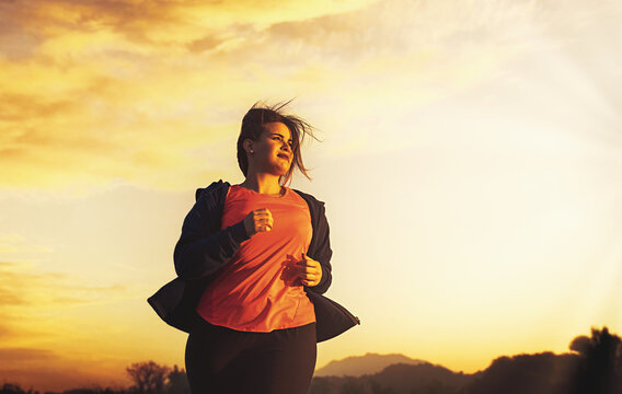 A beautiful curvy young adult woman jogger runs in a nature at sunset - determination and weight loss lifestyle concept