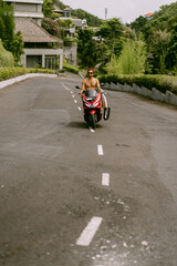 Surfer rides on motorbike with surfboard. Bali island, Indonesia. Young stylish man driving a scooter. Surfer with a surfboard on a rack on a motorcycle.