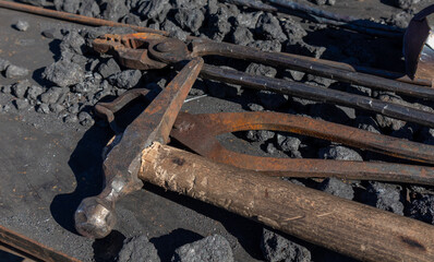 blacksmith tools for hand forging. hammer and tongs on an iron surface among coke