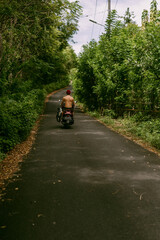 Surfer rides on motorbike with surfboard. Bali island, Indonesia. Young stylish man driving a scooter. Surfer with a surfboard on a rack on a motorcycle.