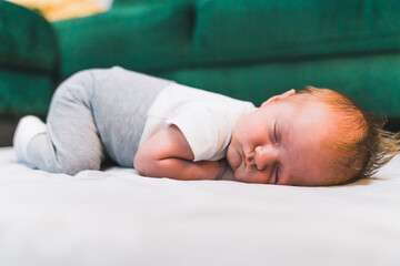 It's time for a baby nap. Cute caucasian infant baby boy in gray sweatpants and white t-shirt sleeping on his belly on soft portable mattress for children. High quality photo
