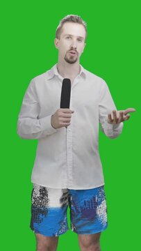 Male reporter in casual shirt and blue shorts hold microphone on green screen 4K