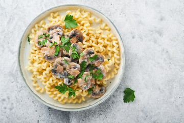 Fusilli pasta with mushrooms, cheese and garlic creamy sauce on plate on on grey stone or concrete table background. Top view. Traditional Italian cuisine.