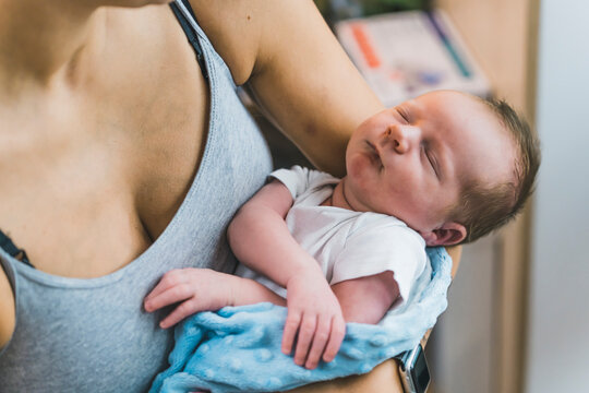 Closeup indoor portrait of adorable cute caucasian infant newborn boy sleeping in the arms of his mother. Little new family member. Childhood concept. High quality photo