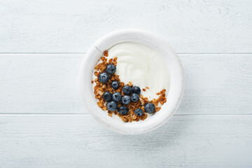 Yogurt. Greek Yogurt with granola and fresh blueberries in white bowl over old white wood background. Morning breakfast concept. Healthy food for breakfast, top view