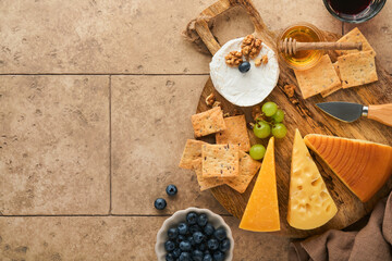 Assortment of cheese, honey, cracker, blueberries, grapes with red and white wine in glasses antipasto server on white marble board on grey background. Cheese plate. Flat lay, copy space.