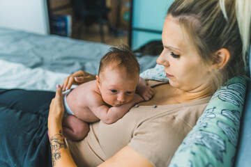 White woman with blond hair resting in bed with her baby boy lying on her chest. Mother bonding with her newborn. Horizontal indoor shot. High quality photo