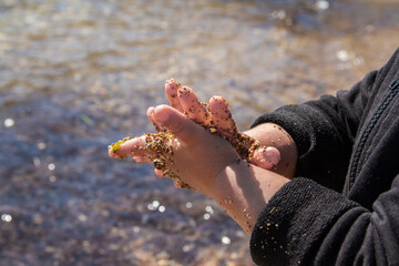 Dirty hands of a toddler playing with sand, water and stones at a beach