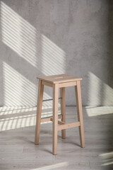 Stołek drewniany na tle ściany z cieniami od żaluzji © Studio Migafka