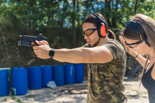 male instructor showing a girl how to hold a pistol with a collimator and a torch correctly, medium shot. High quality photo