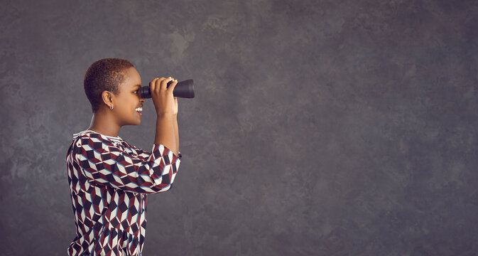 Banner web image of millennial African American woman on black studio background hold binocular glass look at empty mockup copy space. Happy young ethnic girl use optical equipment consider deal.