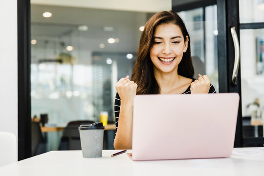 Happy business woman with raised in yes gesture hand, Beautiful young girl smiling celebrating success with arms up in front of laptop, win and exited woman celebrating achievement