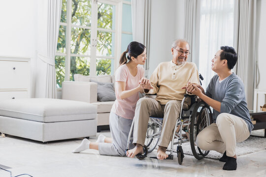 Happy Asian family of senior with beautiful daughter, her husband and grandson take care old man sitting on wheelchair in house, positive dad have strength and positive thinking