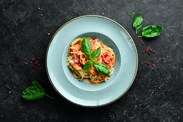 Pasta with chicken fillet, tomatoes and basil in a plate. Italian dish. On a black stone background.