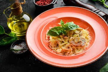 Pasta with chicken fillet, mushrooms, cheese and basil in a plate. Italian dish. On a black stone background.
