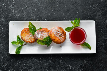 Dessert. Cheese pancakes with raspberry sauce and powdered sugar. On a black stone background.