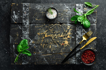 Cooking background: cutlery, spices and basil. On a black stone background.