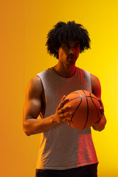 Image of biracial basketball player with basketball on orange to yellow background