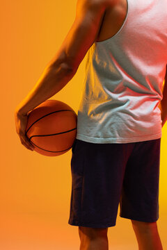 Image of midsection of biracial basketball player with basketball on orange to yellow background