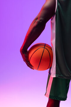 Image of midsection of african american basketball player with basketball on neon purple background