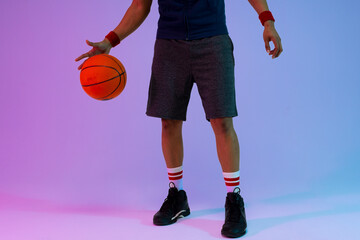Image of low section of biracial basketball player with basketball on purple to blue background - Powered by Adobe