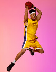 Image of biracial basketball player jumping in the air with basketball on pink background