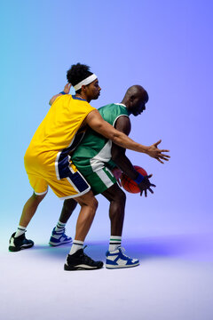 Image of two diverse basketball players with basketball playing on purple to blue background