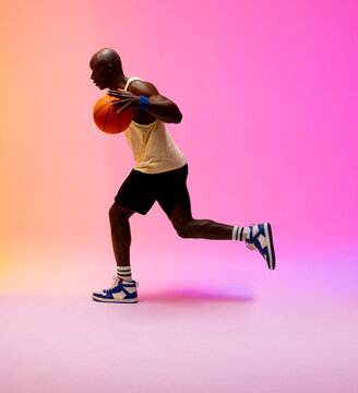 Image of african american basketball player running with basketball on pink to orange background