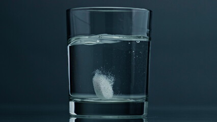 Closeup tablet dropped glass at dark background. Effervescent pill dissolving