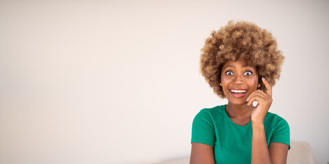 Surprised attractive young dark-skinned woman in green t-shirt beige background looking with big...