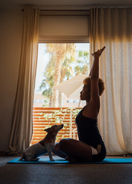 inspirational morning breathing exercises and affirmations. Adorable small dog Jack Russell terrier with love watching the owner woman in sportswear in front of the window with her hands up