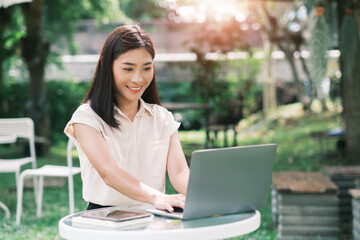 Asian business woman working outside freelancer using computer laptop and digital tablet device wireless remote communication technology, online worker casually enjoying outdoor in nature sunlight.