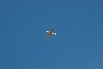 small white ultralight microlight aircraft flying across a bright blue sky