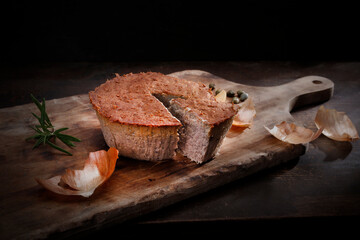 Homemade, baked meat pate. Rustic composition with cut pate on a wooden chopping board, on a black...