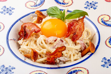 Carbonara pasta with bacon and chanterelles in a decorative plate.