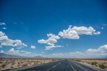 An endless straight paved highway leads through the steppe of Utah USA under blue sky with cheerful white little clouds.
