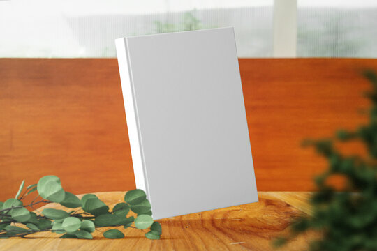 Clean minimal photo book 5.5x8.5 mockup floating on wooden top table with leaves and plant