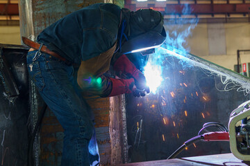 A welder is welding the stiffener of steel structuring with Flux-cored arc welding ( FCAW ), at an industrial factory.
