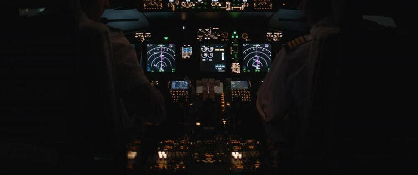 Commercial aircraft pilots performing pre flight check of the jet airplane at night. View from inside the cabin. Real aircraft, nighttime shot
