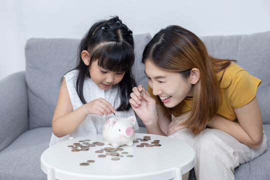 Asian Mother Help Her Daughter Put Coins Money into Piggy Bank