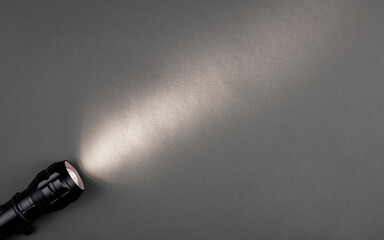 A bright beam of light from a flashlight shines on a gray background - obrazy, fototapety, plakaty