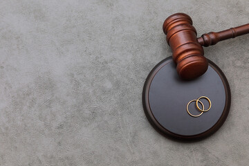 Law theme. Judge gavel wedding rings on concrete stone grey background. Divorce proceedings. Mallet...