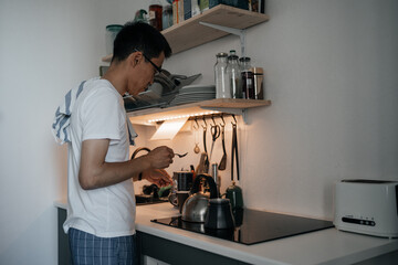 Adult asian man wearing glasses preparing coffee in kitchen at home. Kitchen facilities.