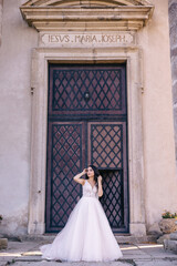 Obraz premium a bride with long black hair and a long dress stands by the black iron door at the entrance to the building.
