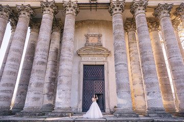 a beautiful bride stands near the big columns and doors of the architecture.