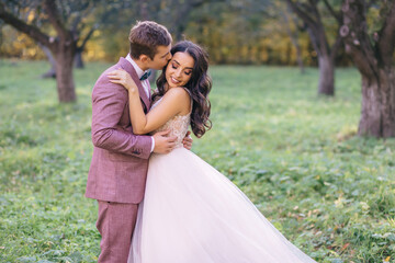 beautiful newlyweds are hugging on the background of trees in the park. bride and groom on a walk in nature.