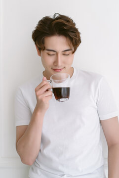 Happy Asian man wearing casual clothes drinking hot coffee standing isolated on white background. Peaceful millennial korean guy relaxing day, chilling on lazy morning enjoy in smell of fresh coffee.